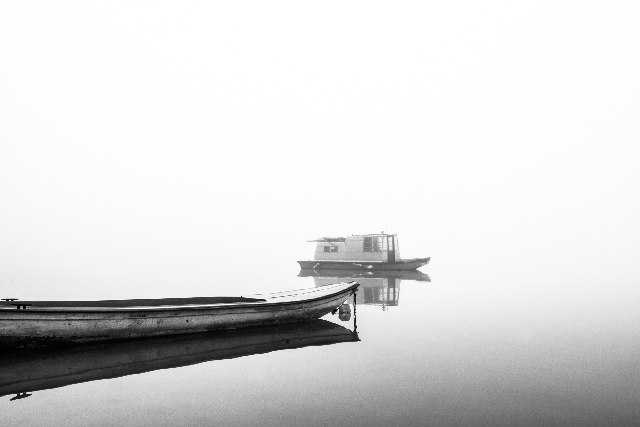 Two boats emerging from a pale fog over still water