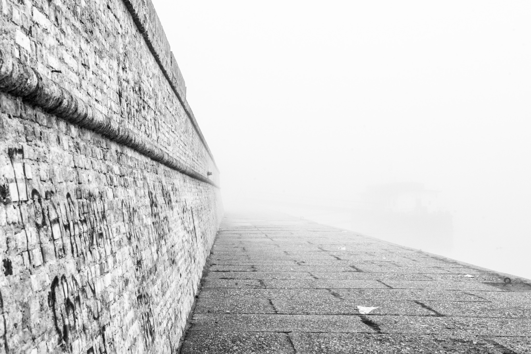 A stone wall and riverside pavement disappearing into fog