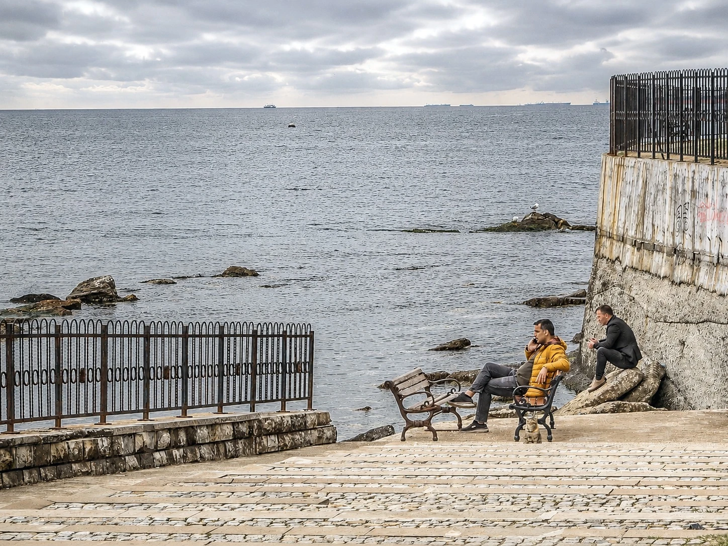 People resting beside the water and a stone wall