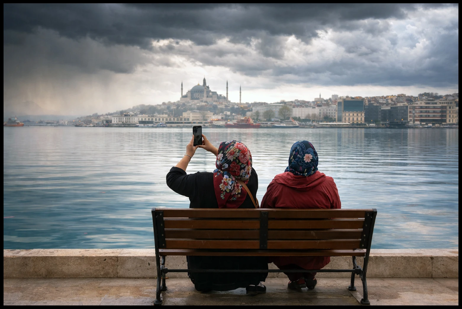 Two women on a waterfront bench beneath gathering clouds