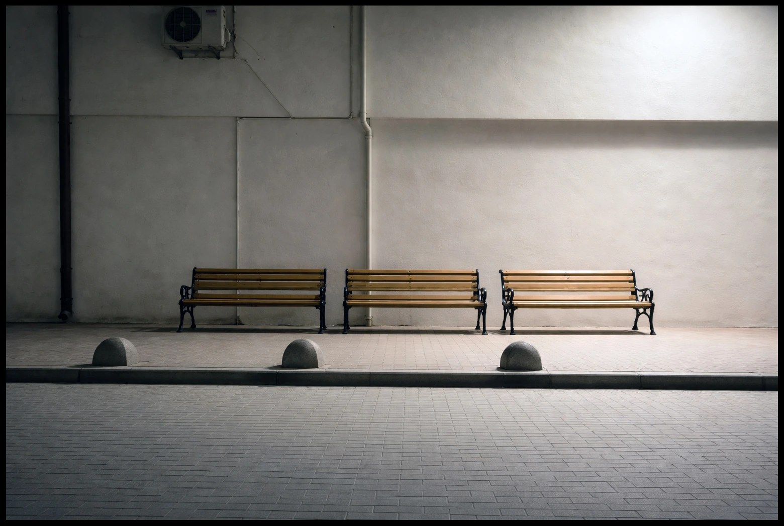 Three empty benches against a wall crossed by deep shadows