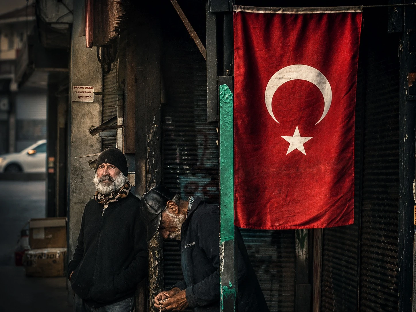 A bearded man beside a Turkish flag on a weathered building