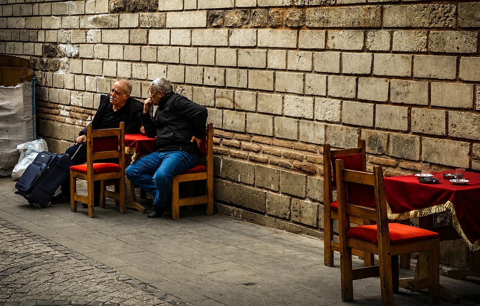 Two people seated at small tables beside a stone wall