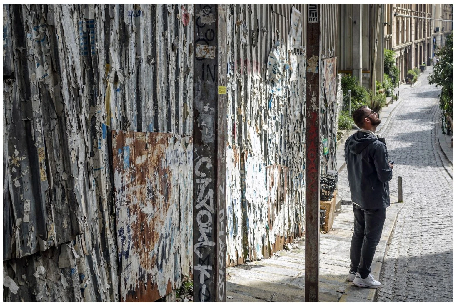 A person looking upward beside weathered metal doors on a narrow street