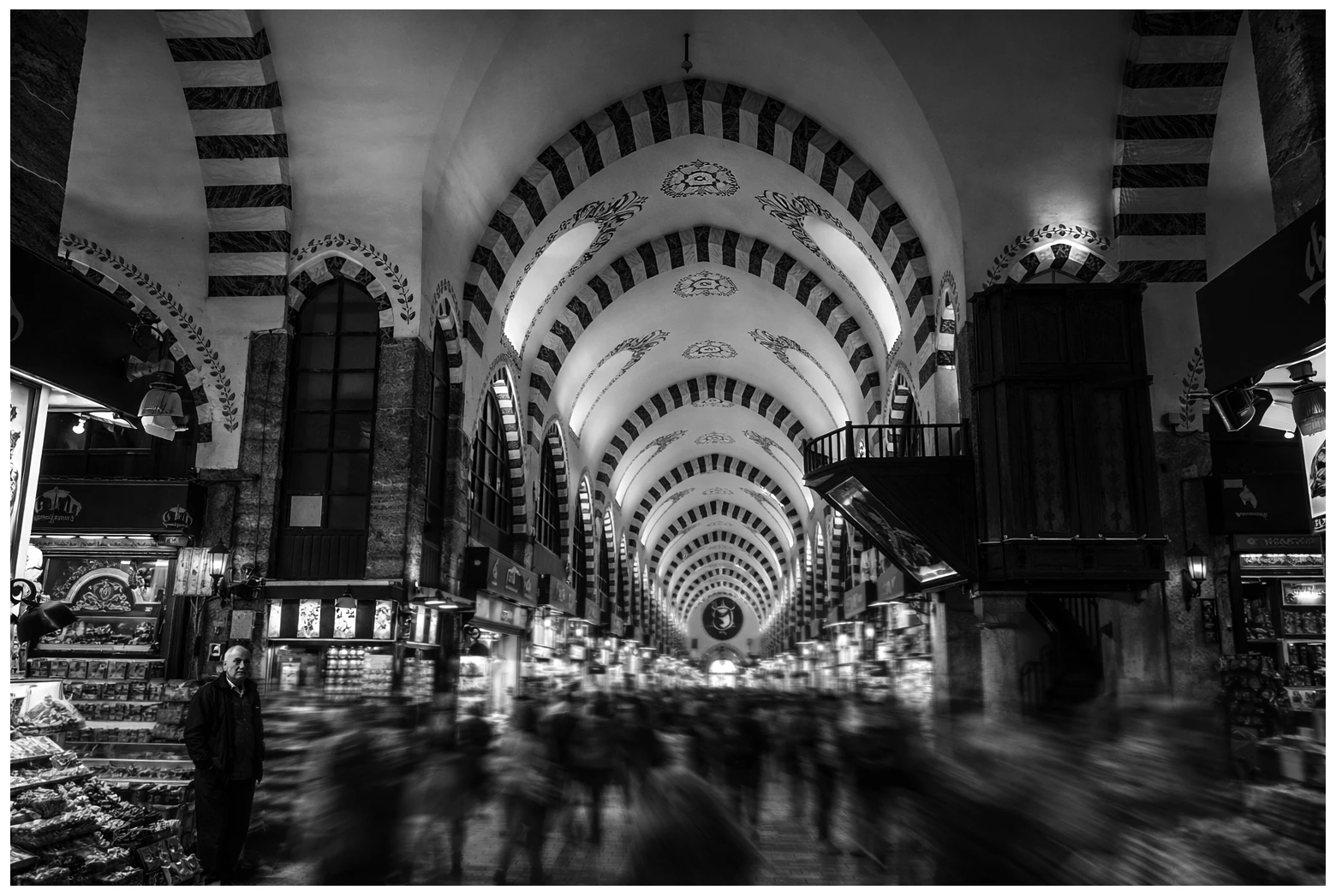A monochrome view of an arched market hall with blurred figures moving through it