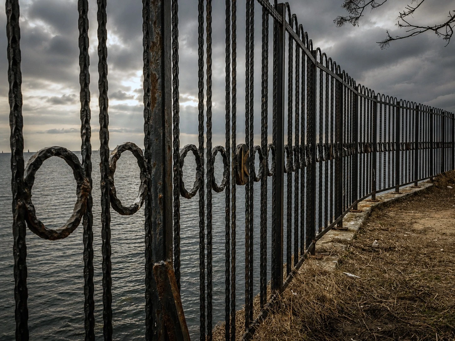 A metal fence beside the sea beneath dramatic clouds