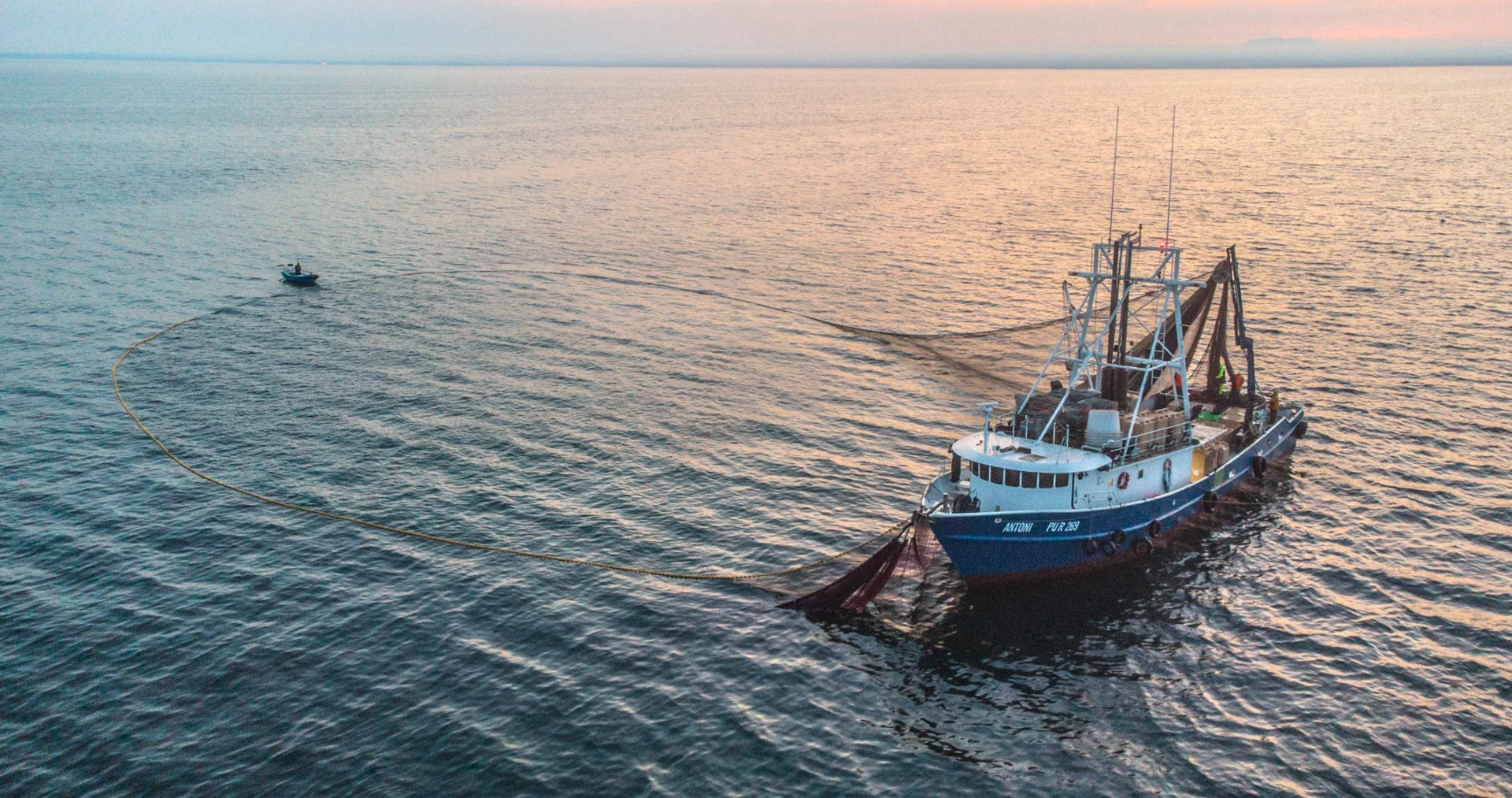 An aerial view of a fishing boat with nets extended on open water