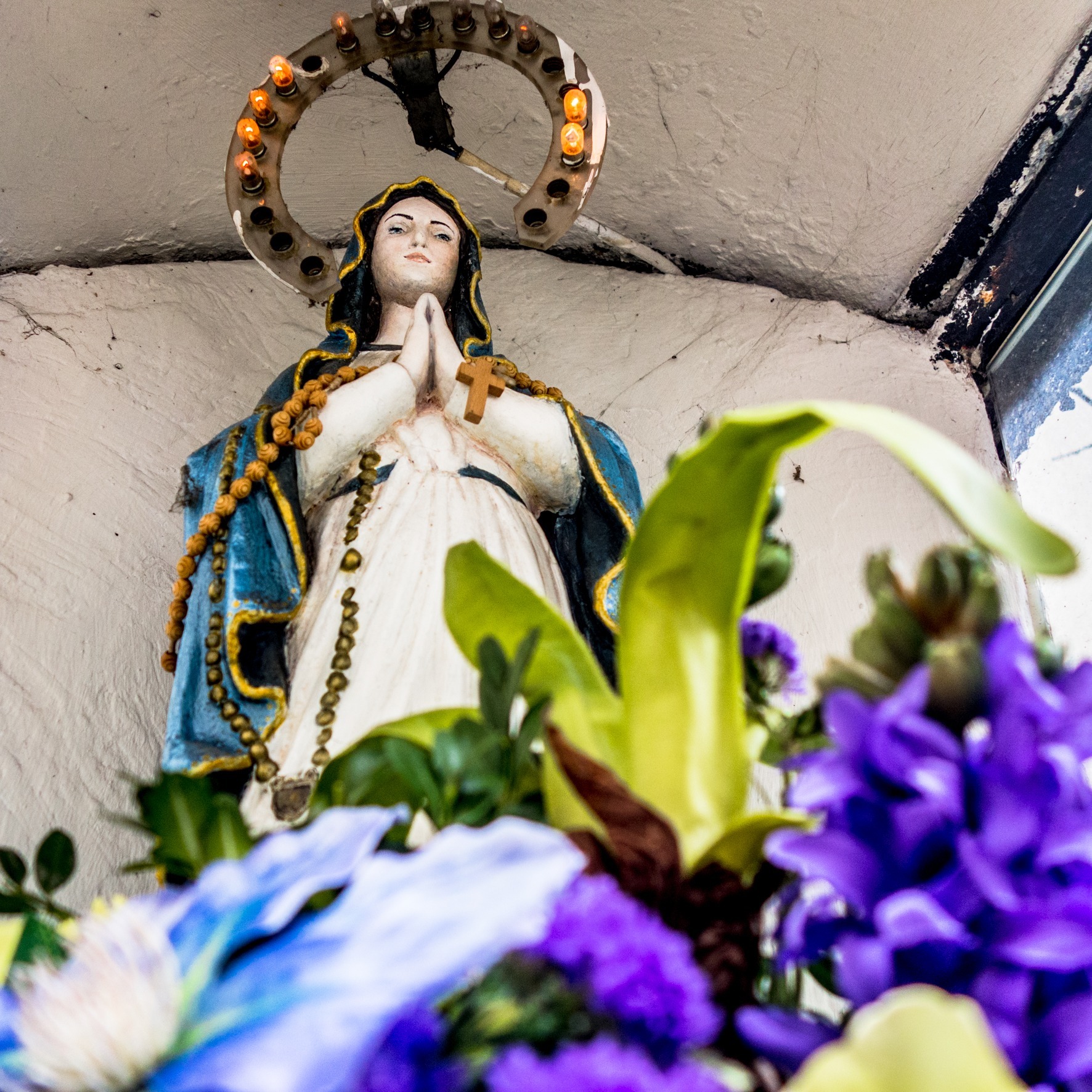 A statue of Mary with a halo and flowers in the foreground