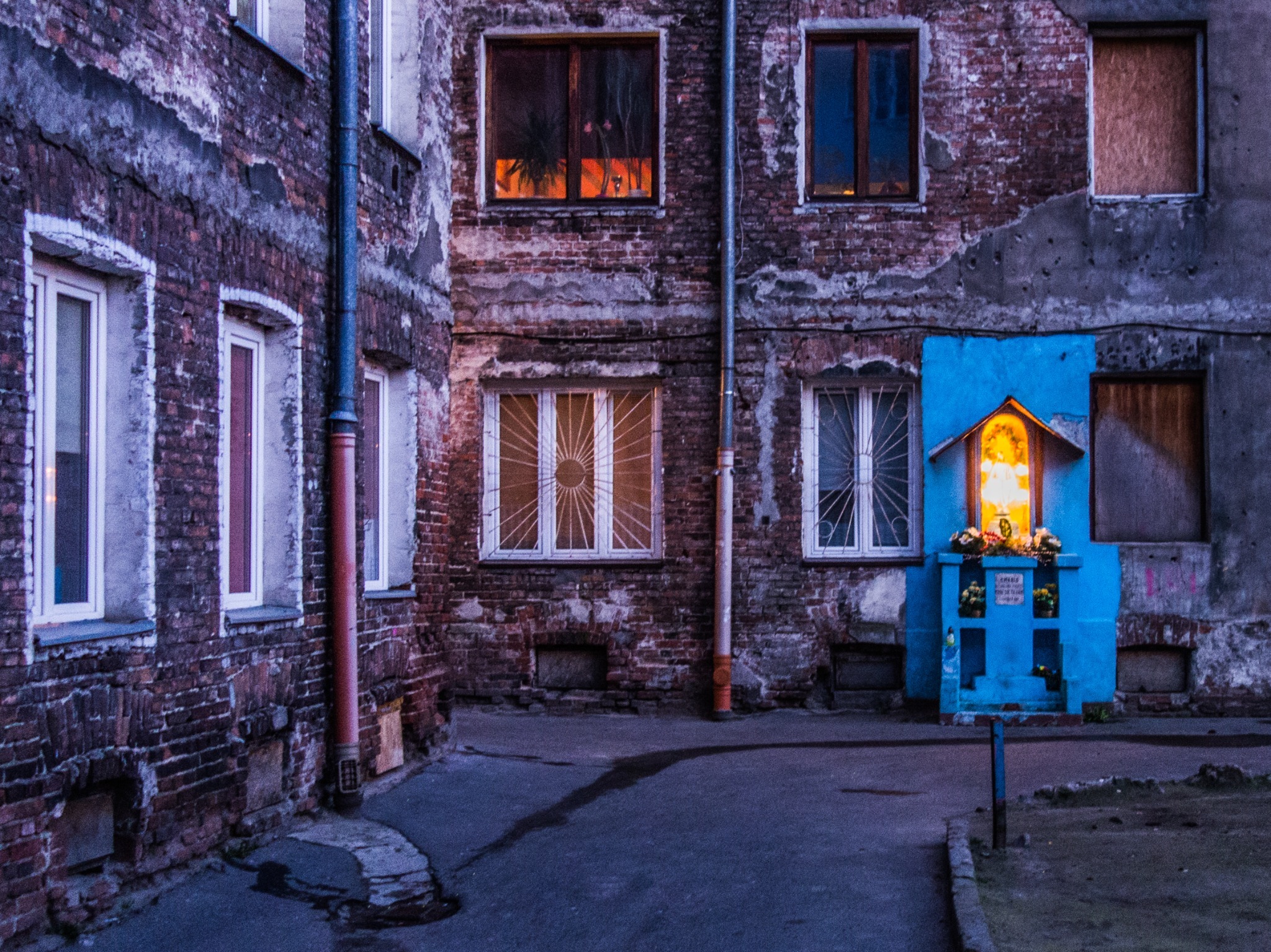 An illuminated blue shrine against the walls of an old courtyard