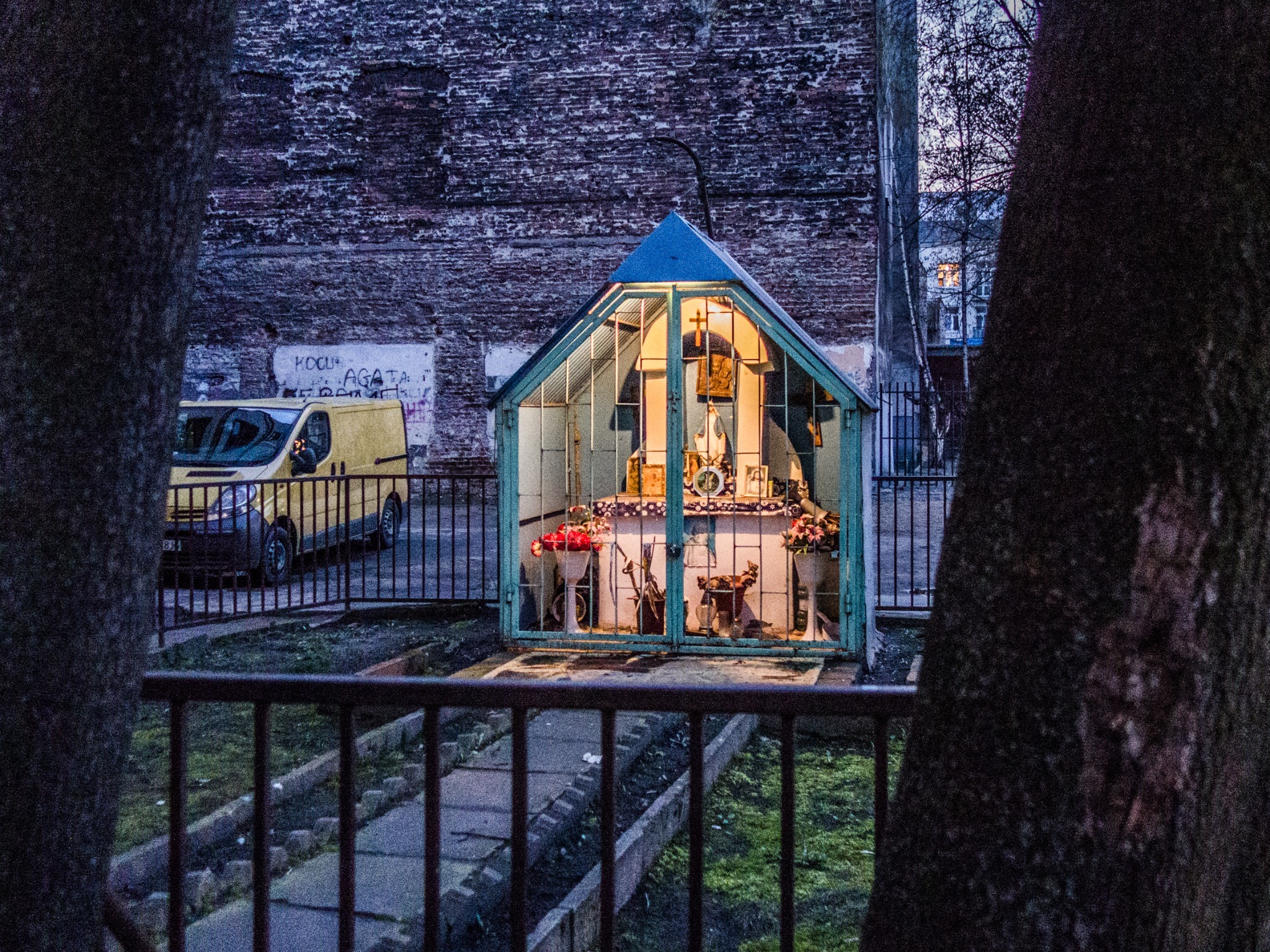 An illuminated glass-fronted shrine beside a tree