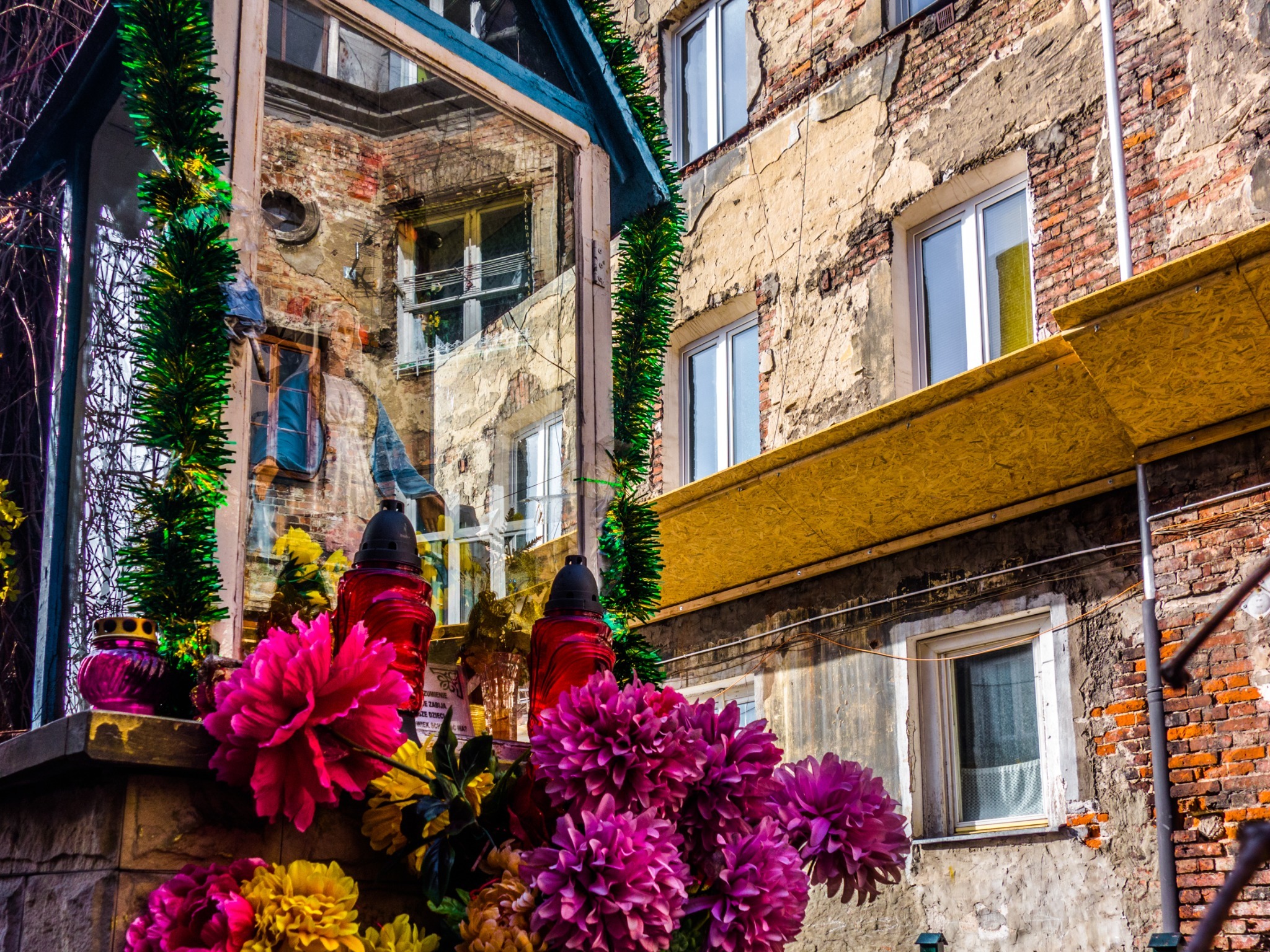 Flowers beneath a glass shrine reflecting courtyard buildings