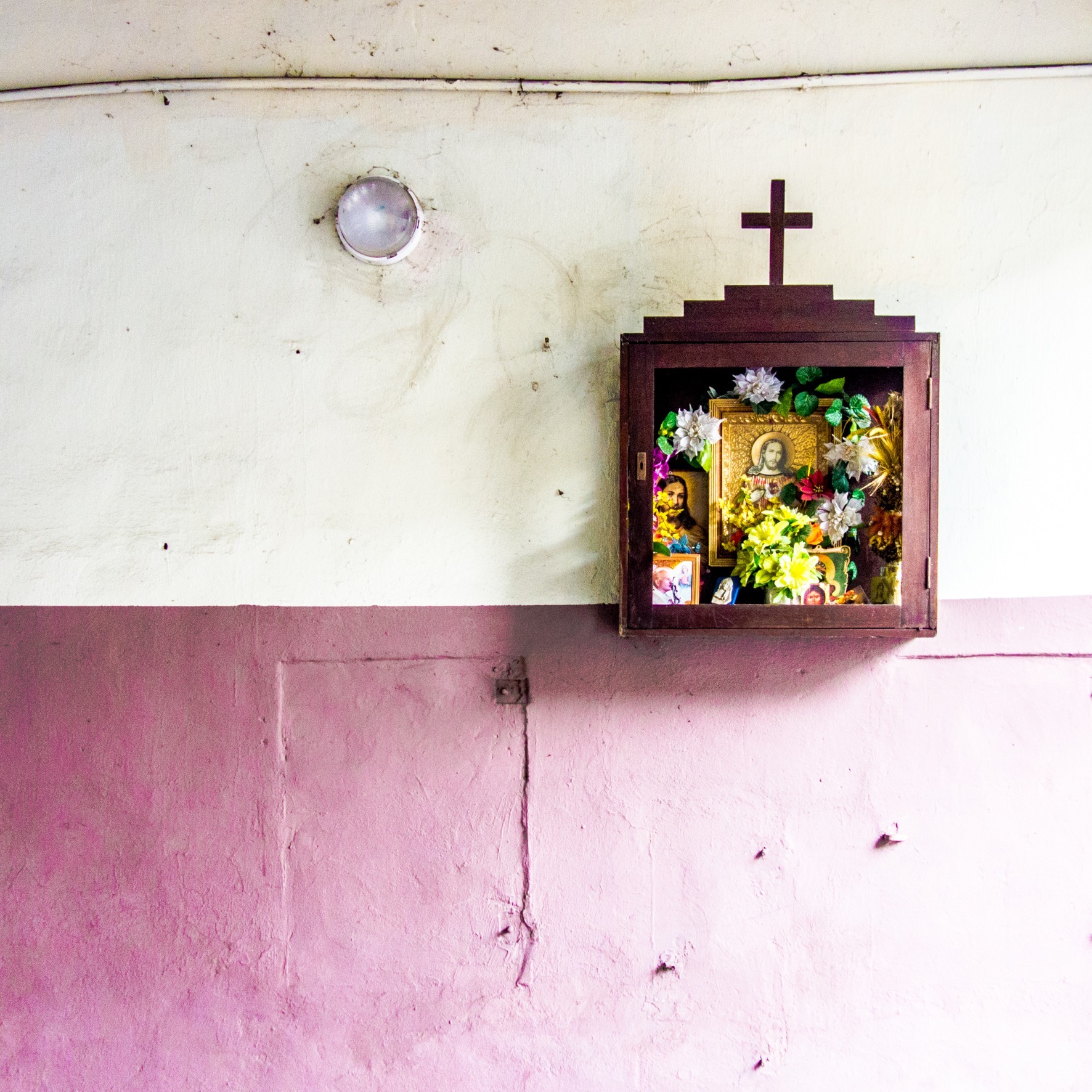 A small wooden shrine with a cross on a white and pink interior wall