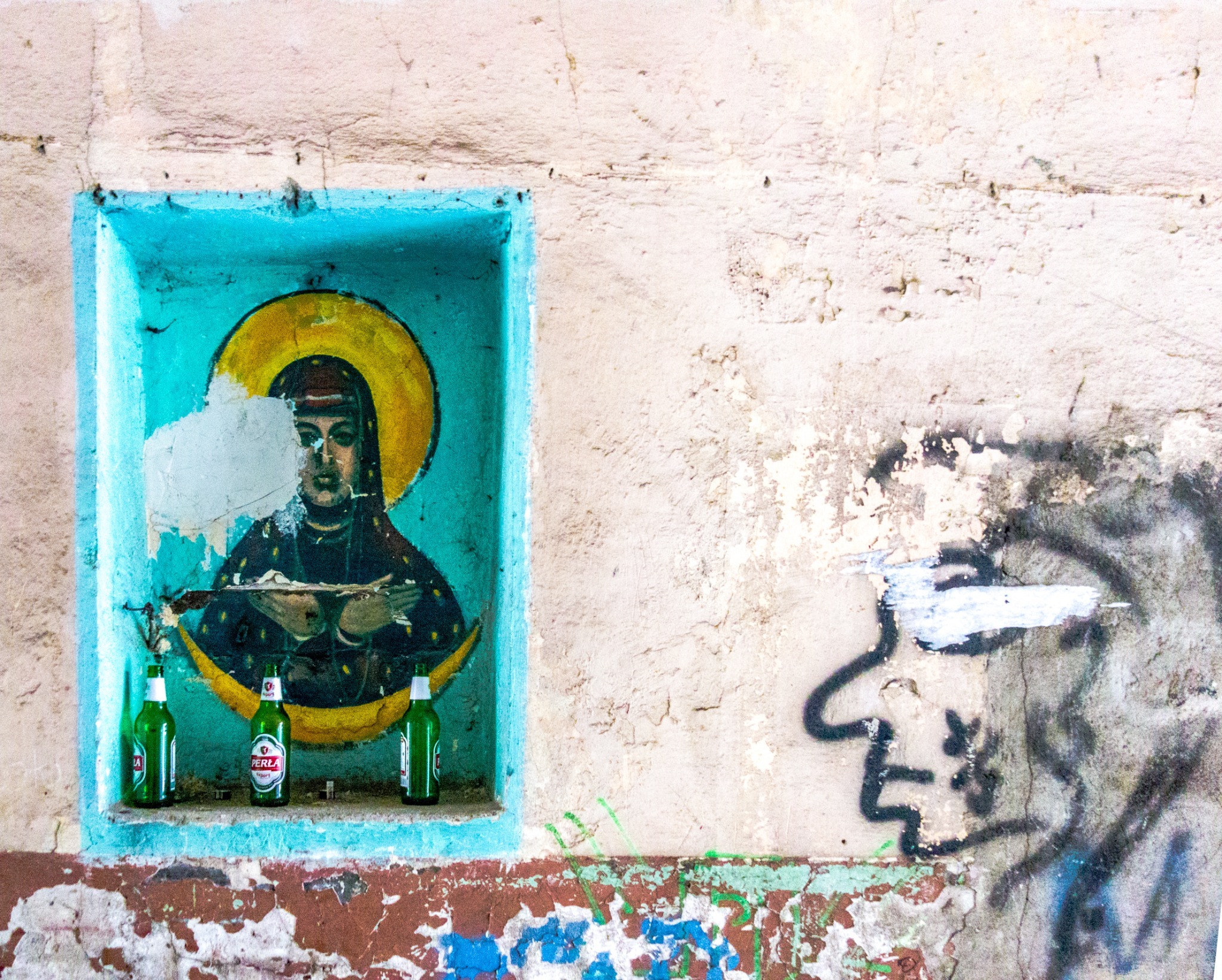 A religious icon in a turquoise wall recess beside graffiti
